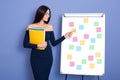 Beautiful young businesswoman holding paper folder in hands, standing near flip chart with stickers, attractive female wearing Royalty Free Stock Photo