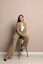 Beautiful young businesswoman sitting on stool near beige wall Royalty Free Stock Photo