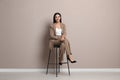 Beautiful young businesswoman sitting on stool near beige wall Royalty Free Stock Photo