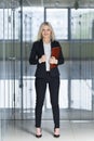 Beautiful young businesswoman smiling and standing with folder in the office. Royalty Free Stock Photo