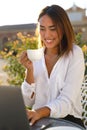 Beautiful young businesswoman or student holding a cup of coffee smiling and typing on laptop Royalty Free Stock Photo