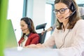 Beautiful young businesswoman using headset with colleagues in background at office Royalty Free Stock Photo
