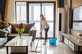 Beautiful young Caucasian blonde housewife cleaning floor in living room. Modern home interior, domestic life Royalty Free Stock Photo