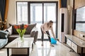 Beautiful young Caucasian blonde housewife cleaning floor in living room. Modern home interior, domestic life Royalty Free Stock Photo