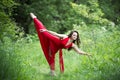 Beautiful young caucasian brunette woman in red dress outdoors, flexibility and stretching on nature