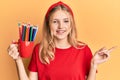 Beautiful young caucasian girl holding art colored pencils smiling happy pointing with hand and finger to the side Royalty Free Stock Photo