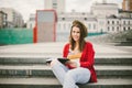 A beautiful, young Caucasian girl sitting on the street smile, the joy, sit with notebook and pen in Ruhi. In the red sweater, jea Royalty Free Stock Photo