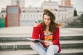 A beautiful, young Caucasian girl sitting on the street smile, the joy, sit with notebook and pen in Ruhi. In the red sweater, jea Royalty Free Stock Photo