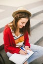 A beautiful, young Caucasian girl sitting on the street smile, the joy, sit with notebook and pen in Ruhi. In the red sweater, jea Royalty Free Stock Photo