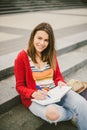 A beautiful, young Caucasian girl sitting on the street smile, the joy, sit with notebook and pen in Ruhi. In the red sweater, jea Royalty Free Stock Photo