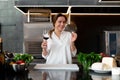 Beautiful young caucasian girl standing in kitchen in a white uniform smiling and tasting red wine Royalty Free Stock Photo