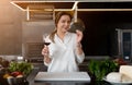 Beautiful young caucasian girl standing in kitchen in a white uniform smiling and tasting red wine Royalty Free Stock Photo