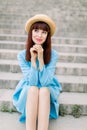 Beautiful young caucasian girl in urban background, sitting on stairs. Pretty red haired girl wearing hat and blue dress Royalty Free Stock Photo
