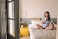 Beautiful young caucasian girl wears pajamas looking out window sits on bed. Royalty Free Stock Photo