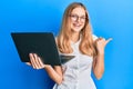 Beautiful young caucasian girl working using computer laptop pointing thumb up to the side smiling happy with open mouth Royalty Free Stock Photo