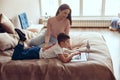 Beautiful young Caucasian mother sitting on bed and watching small son using laptop. Royalty Free Stock Photo