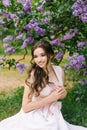 A beautiful young Caucasian smiling happy girl with professional makeup in a delicate pink dress sits near a Bush of blooming Royalty Free Stock Photo