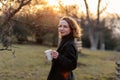 Beautiful young Caucasian woman enjoy sunny spring day, park cherry garden, romantic portrait, drinking coffee, lady in black coat Royalty Free Stock Photo