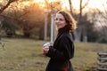 Beautiful young Caucasian woman enjoy sunny spring day, park cherry garden, romantic portrait, drinking coffee, lady in black coat Royalty Free Stock Photo