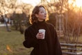 Beautiful young Caucasian woman enjoy sunny spring day, park cherry garden, romantic portrait, drinking coffee, lady in black coat Royalty Free Stock Photo