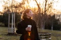 Beautiful young Caucasian woman enjoy sunny spring day, park cherry garden, romantic portrait, drinking coffee, lady in black coat Royalty Free Stock Photo