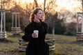 Beautiful young Caucasian woman enjoy sunny spring day, park cherry garden, romantic portrait, drinking coffee, lady in black coat Royalty Free Stock Photo