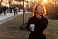 Beautiful young Caucasian woman enjoy sunny spring day, park cherry garden, romantic portrait, drinking coffee, lady in black coat Royalty Free Stock Photo