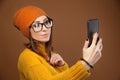 Beautiful young caucasian woman with flowing hair wearing glasses sweater and hat taking a selfie with your smartphone