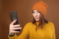 Beautiful young caucasian woman with flowing hair wearing sweater and hat taking a selfie with your smartphone. Studio