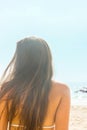 Beautiful young caucasian woman girl with long chestnut hair golden tan in white swimming suits sits on beach looking at sea Royalty Free Stock Photo