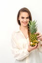 Beautiful young Caucasian woman holding pineapple and smiling, wearing a white shirt over white background. Royalty Free Stock Photo