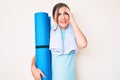 Beautiful young caucasian woman holding yoga mat stressed and frustrated with hand on head, surprised and angry face Royalty Free Stock Photo