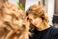 The beautiful young caucasian woman looks at her reflection in the mirror checking hairstyle and makeup in a beauty Royalty Free Stock Photo