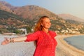 A beautiful young Caucasian woman in a pink blouse with red hair smiles and enjoys the sunset against the background of the Medite Royalty Free Stock Photo