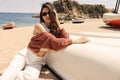 Beautiful young caucasian woman posing near white upside down boat with sea in background. Royalty Free Stock Photo