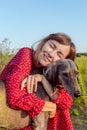 A beautiful young Caucasian woman in a red dress hugs her pet, a gray purebred dog, in the park