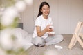 Beautiful young caucasian woman sitting on bed and choosig which cream use to moisturise her face.