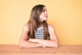 Beautiful young caucasian woman wearing casual clothes sitting on the table looking to side, relax profile pose with natural face Royalty Free Stock Photo