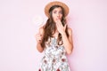 Beautiful young caucasian woman wearing summer hat and lollipop covering mouth with hand, shocked and afraid for mistake Royalty Free Stock Photo
