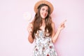 Beautiful young caucasian woman wearing summer hat and lollipop smiling happy pointing with hand and finger to the side Royalty Free Stock Photo
