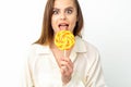 Beautiful young caucasian woman wearing a white shirt licking a lollipop on a white background. Royalty Free Stock Photo