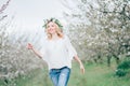 Beautiful young cheerful pregnant woman in wreath of flowers on head touching belly while walking in spring tree garden. Beauty Royalty Free Stock Photo