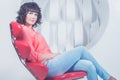 Beautiful young confident woman sitting in red chair against white wall Royalty Free Stock Photo