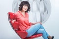 Beautiful young confident woman sitting in red chair against white wall Royalty Free Stock Photo
