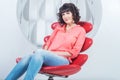 Beautiful young confident woman sitting in red chair against white wall Royalty Free Stock Photo