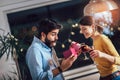 Young couple is celebrating at home. Pretty girl is giving her boyfriend a gift box Royalty Free Stock Photo