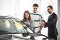 Beautiful young couple choosing a car at the dealership talking to the salon manager with tablet in hands Royalty Free Stock Photo