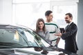 Beautiful young couple choosing a car at the dealership talking to the salon manager with tablet in hands Royalty Free Stock Photo