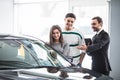 Beautiful young couple choosing a car at the dealership talking to the salon manager with tablet in hands Royalty Free Stock Photo