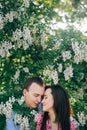 Beautiful young couple gently hugging in green leaves and white flowers in spring garden in sunshine. Happy family embracing at